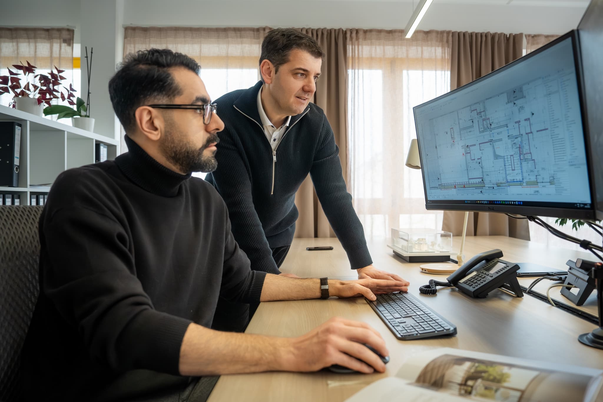Deux collaborateurs d'ACOM revoyant un plan en CAO sur l'écran de l'atelier.