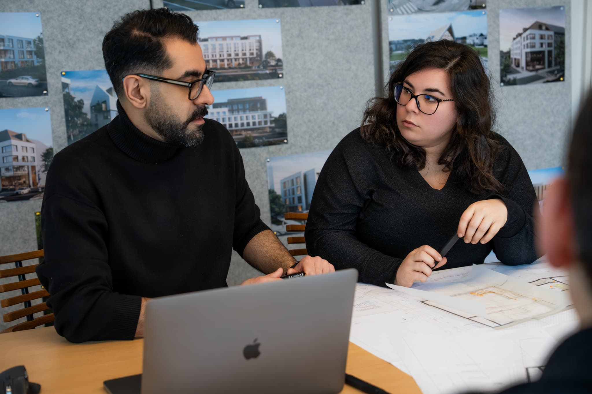 Échange entre architectes d'ACOM devant le mur de projets de l'atelier.